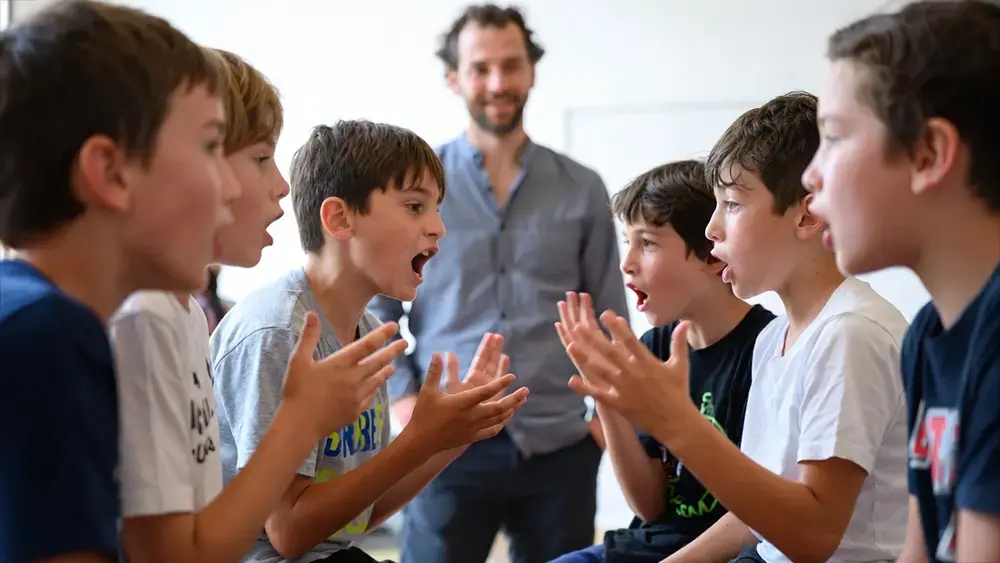 Enfants de 8 à 11 ans en pleine discussion animée pendant un cercle de parole pour résoudre un conflit en périscolaire, avec un animateur en arrière-plan qui observe