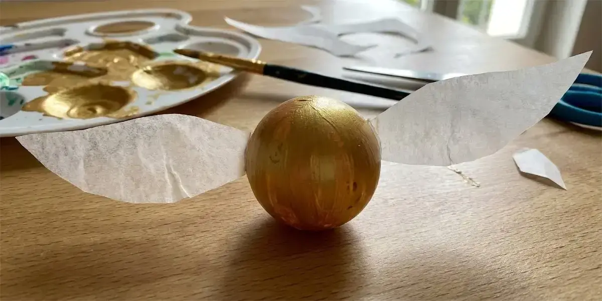Activité manuelle pour enfant : Vif d'Or de l'univers Harry Potter fait main en peinture dorée et papier calque posé sur une table de bricolage avec matériel créatif